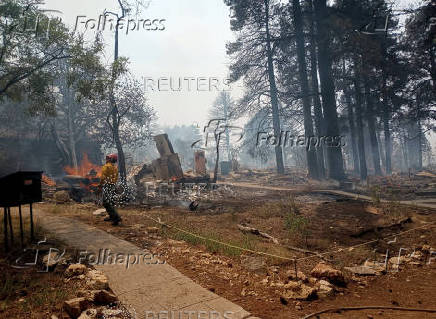 A firefighter stands near smoldering debris and active flames amid the charred remains of a burned structure near the Grand Canyon Lodge