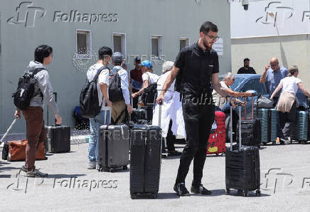 Expats, including diplomats from different nationalities, who were stranded in West Bank and Israel, wait as they hold belongings while being evacuated through the King Hussein Bridge crossing, in South Shuna