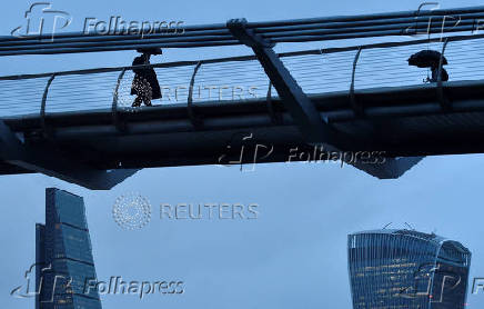 FILE PHOTO: City workers cross the Millennium footbridge in the financial district of London