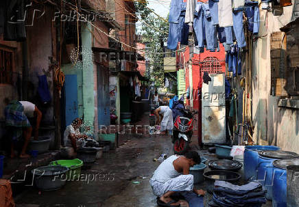 People wash clothes as pairs of jeans hang out to dry before they are sold in a wholesale market in Kolkata