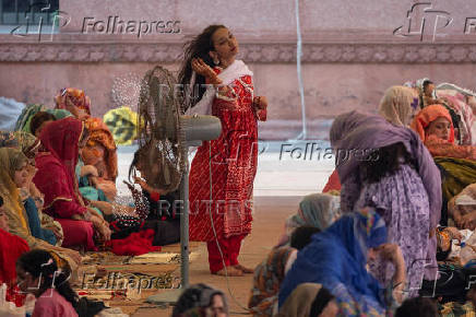 Woman stands near fan to cool off ahead of Eid al-Adha prayer in Lahore