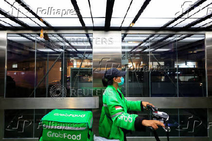 FILE PHOTO: A driver working for the ridesharing company Grab holds a bicycle as she delivers food in Jakarta