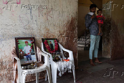 A family member with a child, stands next to photo of Akash Patni, who died after an Air India Boeing 787-8 Dreamliner plane crashed during takeoff from an airport, in Ahmedabad