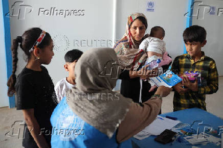 An Afghan woman deported from Iran, registers her children for vaccination inside a WHO tent at a camp for returning migrants near the Islam Qala border crossing