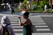 A person holds up a fan to cover her face from sunlight amid a yellow alert for heat, in Shanghai