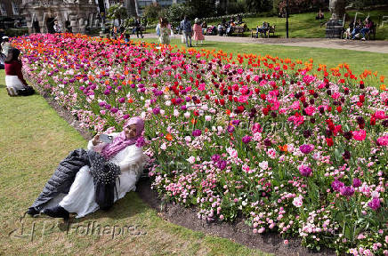 A woman poses next to blooming flowers in Victoria Embankment Gardens, London