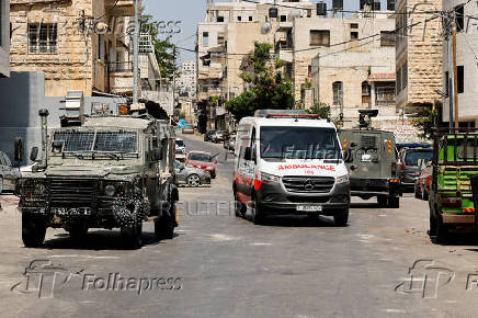 An ambulance drives next to an Israeli military vehicle during an Israeli raid in Nablus