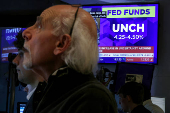 A screen displays the Fed rate announcement as traders work on the floor of the NYSE in New York
