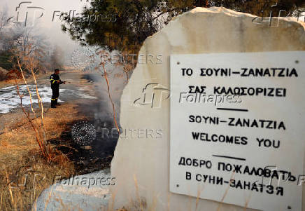 A firefighter uses a hose to cool a burnt area during a wildfire at the area of Souni, near Limassol
