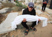 A mourner carries the body of a child from the Al-Arabeed family killed in Israeli strikes, at a cemetery, in Gaza City
