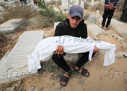A mourner carries the body of a child from the Al-Arabeed family killed in Israeli strikes, at a cemetery, in Gaza City