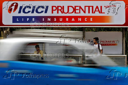 FILE PHOTO: Passengers wait in front of an ICICI Prudential billboard at a bus stop in Mumbai