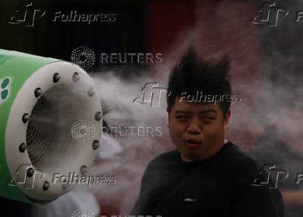 A tourist cools off in front of a misting fan near a venue of the Hozuki-Ichi (Japanese lantern plant fair), at Sensoji temple, in Tokyo
