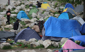 A migrant walks towards tents in a small camp carrying food distributed by a charity in Calais, France