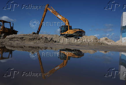 An excavator is reflected in seawater after big waves hit Rio de Janeiro