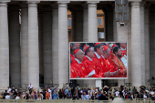 People watch a Holy Mass on a large sceen in Saint Peter's Square