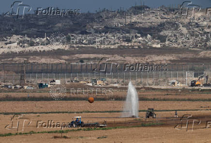Farmers work in a field on the Israeli side of the Israel Gaza border