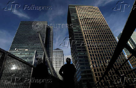 FILE PHOTO: Silhouetted workers walk in front of office towers in the Canary Wharf financial district in London