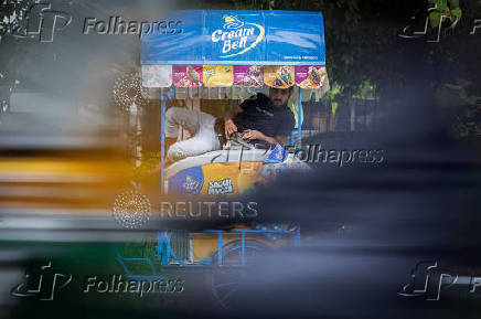 An ice-cream vendor takes shelter in his cart as it rains in New Delhi