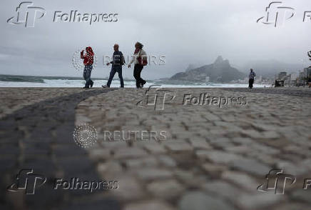People walk along the Arpoador beach amid strong winds in Rio de Janeiro