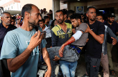 A Palestinian carries a man who was wounded in an Israeli strike while waiting for aid, according to the Gaza Health Ministry, at Nasser hospital, in Khan Younis