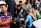 A Palestinian carries a man who was wounded in an Israeli strike while waiting for aid, according to the Gaza Health Ministry, at Nasser hospital, in Khan Younis