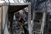 A man sits near the remains of his burned house after a fire at a slum area in Rohini