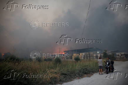 People watch a fire at a cement factory sparked by a nearby wildfire, in Patras