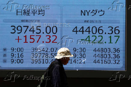 A man walks in front of a screen displaying Japan's Nikkei share average and the Dow Jones Industrial Average outside a brokerage in Tokyo