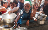 Palestinians wait to receive food cooked by a charity kitchen, in Khan Younis