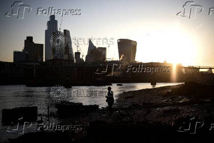 FILE PHOTO: A person stands on the bank of the River Thames during sunrise in London