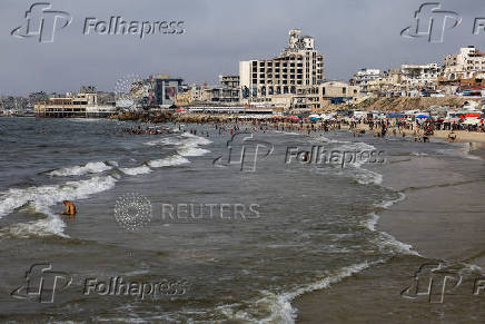 Palestinians, predominately displaced by the Israeli offensive, cool off in the seawater amid summer heat, in Gaza City