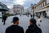 Two men rest on a bench as they look at people passing by in Moscow