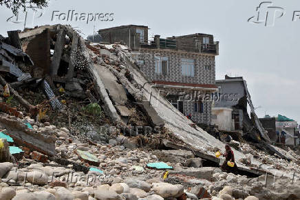 A woman carries plastic cans that she found in the debris of her flood-damaged house on the banks of Tawi river following heavy rain in Jammu