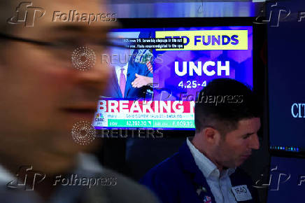 A screen displays the Fed rate announcement as traders work on the floor of the NYSE in New York