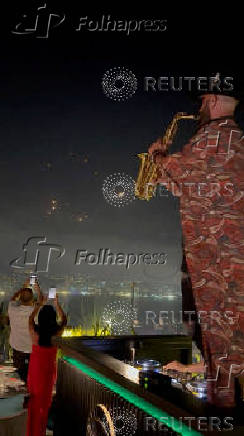 People record the missiles using their phones while a saxophonist plays the instrument, in Kfar Yassine
