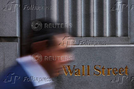 FILE PHOTO: A man walks past a Wall Street marking outside the New York Stock Exchange (NYSE) building on Tuesday following Monday?s broad sell off in New York City