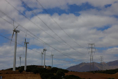 Wind turbines spin next to power lines connecting pylons of high-tension electricity, near Casares