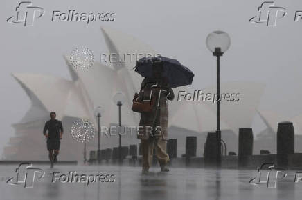 A person carrying an umbrella shelters from the rain as they walk past the Sydney Opera House