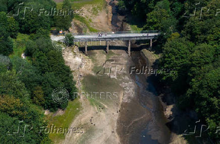 A drone view of people walking over a bridge across a partially dried section of the Jumbles Reservoir near Blackburn