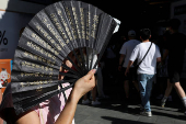 FILE PHOTO: A person holds up a fan to cover her face from sunlight amid a yellow alert for heat, in Shanghai
