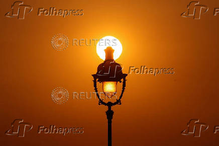 The sun sets behind a street lamp