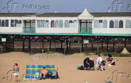People sit on the beach in front of the pier at St Annes