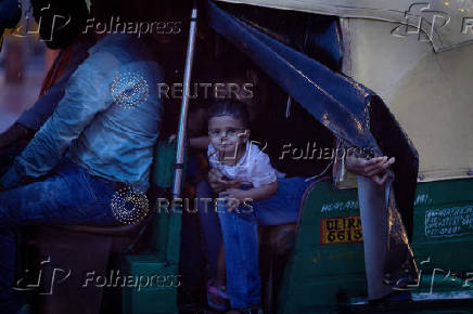 A child looks out from an autorickshaw as it rains rains in New Delhi