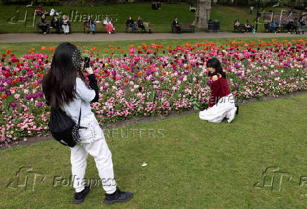 A woman poses next to blooming flowers in Victoria Embankment Gardens, London