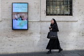 A nun walks past a screen displaying an image of the newly elected Pope Leo XIV near the Vatican