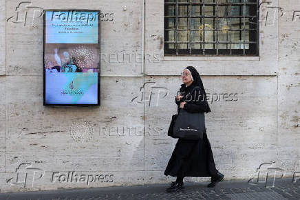 A nun walks past a screen displaying an image of the newly elected Pope Leo XIV near the Vatican