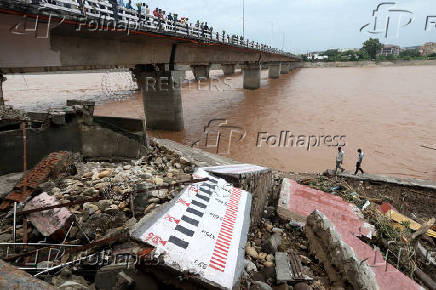 Men walk past a damaged watermark along the banks of the Tawi river following heavy rain in Jammu