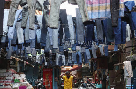 A man walks past pairs of jeans hanging to dry before they are sold in a wholesale market in Kolkata