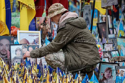 Person in military uniform puts flag at the makeshift memorial to fallen Ukrainian defenders at Independence Square in Kyiv